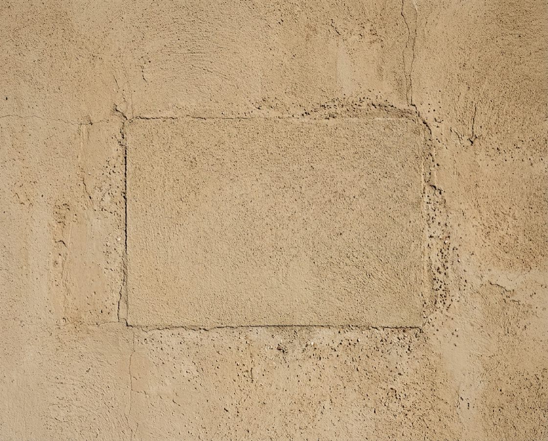 Sección reparada de una pared de estuco mezclada con el acabado desgastado que la rodea, con la orilla del parche apenas visible contra el color viejo